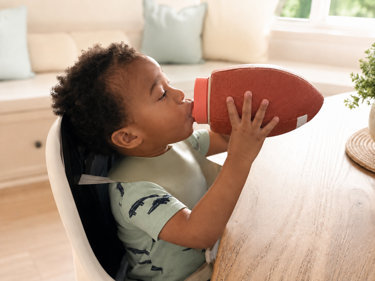 Toddler drinking from a football-shaped Pro-Hands Sports Bottle at a table.